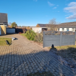 Have med delvist færdiggjort hegn i Hjørring på en solrig dag. De mørke stolper og begyndelsen af hegnet står i kontrast til den blå himmel og grønne have.