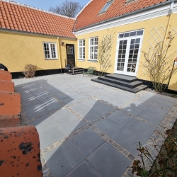 Flisebelagt terrasse ved et gult hus i Aalborg, med rene linjer og moderne belægning, der giver et pænt og funktionelt udendørsområde.