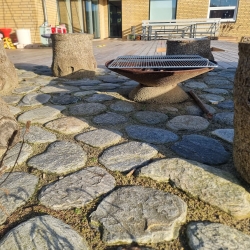 Belægning af natursten omkring en siddeplads i haven i Hjørring. Stenene skaber et hyggeligt og afslappende udemiljø.