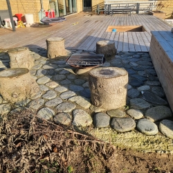 Naturstensbelægning omkring stole i haven i Hjørring, der giver et robust underlag og tilføjer et rustikt element til omgivelserne.