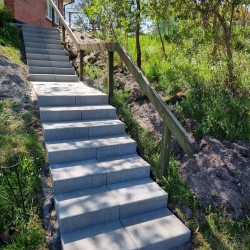 Trappe omgivet af grønne omgivelser i Hjørring, der leder op til en terrasse ved husets indgang, med bredde fliser som belægning.