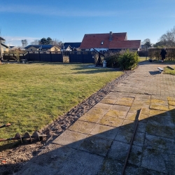 Grønt græsareal i Hjørring omgivet af et solidt, mørkt hegn. Opsætningen af hegnet tilføjer privatliv til haven og skaber en hyggelig atmosfære.