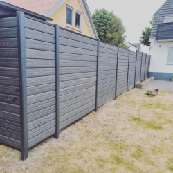 Langt, sort hegn, der løber langs kanten af en have i Hjørring. Hegnet giver et stilfuldt og moderne udseende i uderummet.