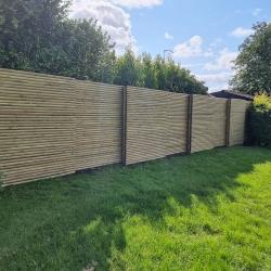 Lyst træhegn langs en grøn have i Hjørring. Hegnet giver et naturligt look og harmonerer med de omgivende buske og træer