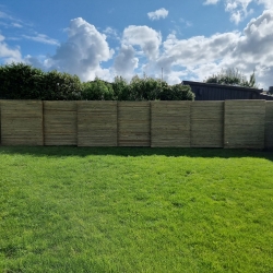 Højt træhegn i baghaven i Hjørring, der giver privatliv og skaber en naturlig baggrund til det grønne græsareal.