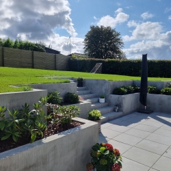 Høj terrasse med blomsterbede og træhegn i baggrunden, hvilket skaber en harmonisk overgang mellem terrasse og græsareal i Aalborg.