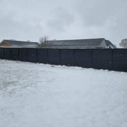 Snedækket have i Aalborg med et solidt sort hegn i baggrunden. Hegnet står stabilt i vinterlandskabet.