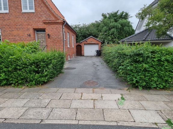 Velholdt hæk langs en indkørsel og fortov i Aalborg, der viser havedesignets fokus på enkelhed og vedligeholdelse.