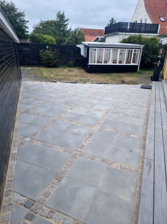  errasse med firkantede fliser, der er lagt i et moderne mønster. Den nye belægning skaber et stilrent udendørs område i Aalborg.