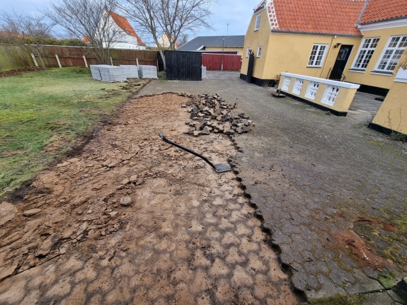 Område i Aalborg, hvor gamle fliser er ved at blive fjernet for at gøre plads til ny belægning, hvilket forbedrer gårdens udseende.