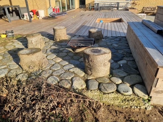  Naturstensbelægning omkring stole i haven i Hjørring, der giver et robust underlag og tilføjer et rustikt element til omgivelserne.