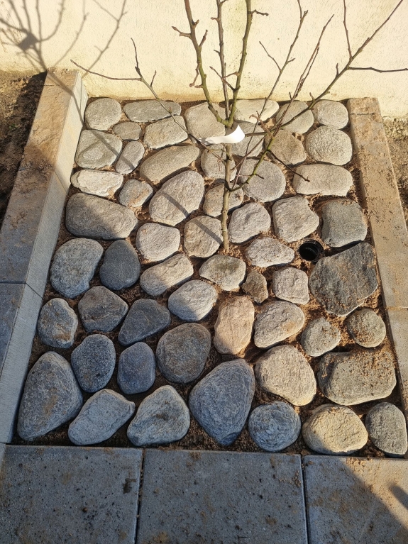 Natursten som belægning i Hjørring, der giver et rustikt look til haven og skaber en naturlig overgang mellem græs og fliser.