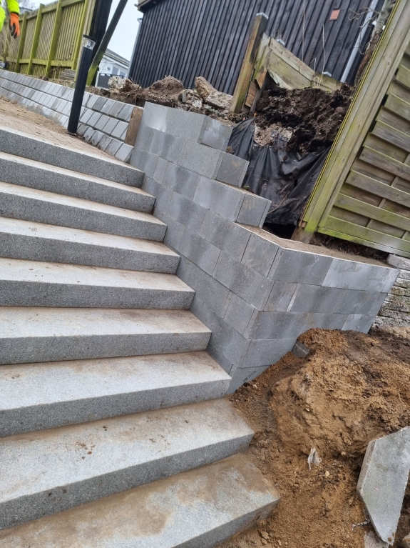 Nybygget trappe med støttevæg langs en skråning i Hjørring, hvor fliser og mursten giver en robust og sikker passage.
