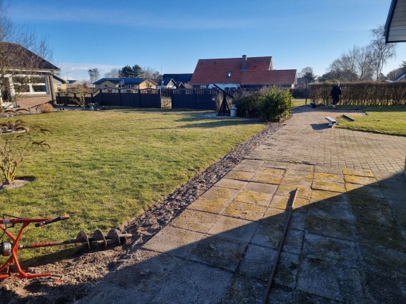 Grønt græsareal i Hjørring omgivet af et solidt, mørkt hegn. Opsætningen af hegnet tilføjer privatliv til haven og skaber en hyggelig atmosfære. 