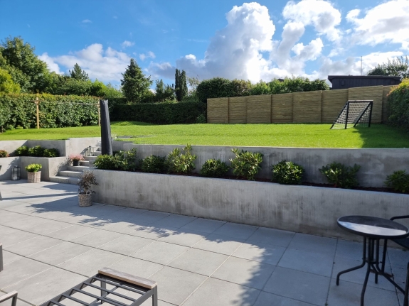 Terrasse omgivet af planter med et træhegn i baggrunden, der afgrænser haven i Aalborg og skaber en hyggelig atmosfære.
