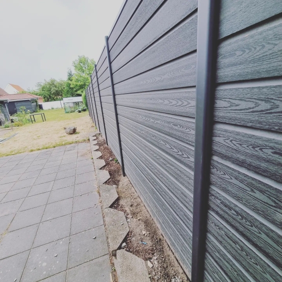 Langt hegn langs kanten af en græsplæne og terrasse i Hjørring. Hegnet giver struktur til haven og skaber et privat udendørs område.