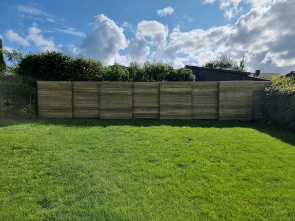 Højt træhegn i baghaven i Hjørring, der giver privatliv og skaber en naturlig baggrund til det grønne græsareal.