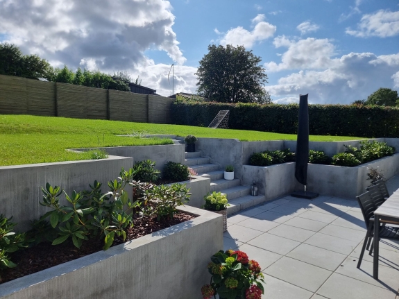 Høj terrasse med blomsterbede og træhegn i baggrunden, hvilket skaber en harmonisk overgang mellem terrasse og græsareal i Aalborg.