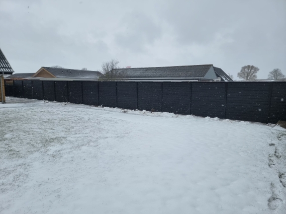 Snedækket have i Aalborg med et solidt sort hegn i baggrunden. Hegnet står stabilt i vinterlandskabet. 